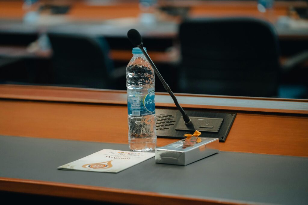 الندوة الفنية والتعليمية لسونودا كيوكوشين – غرب آسيا 2026 Conference table setup in Thailand with bottled water, microphone, and documents. Ideal for business themes.